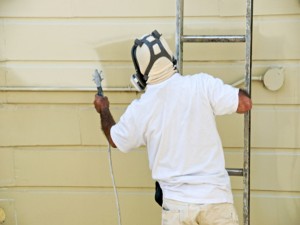 A man on a ladder uses spray gun to paint the exterior of a wooden building